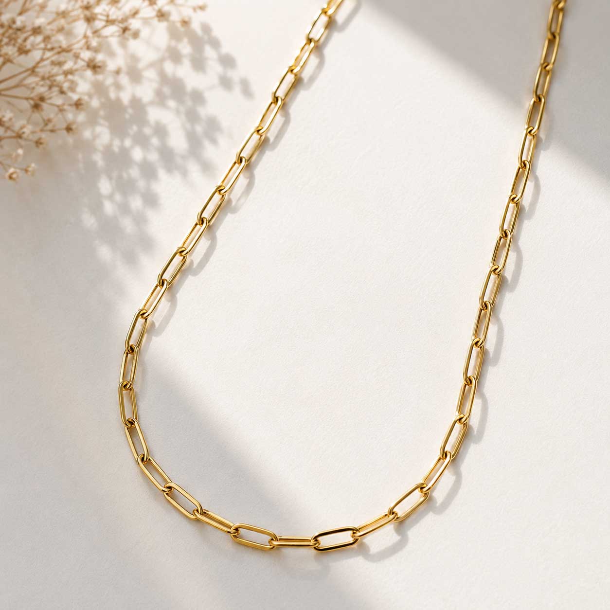 Goldene Paperclip-Halskette auf hellem Untergrund mit Schleierkraut, vergoldete Gliederkette aus Edelstahl mit länglichen Ösen

