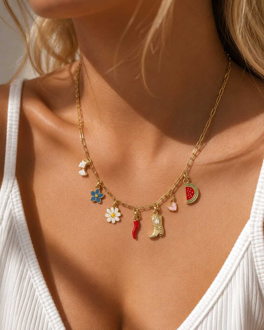 Goldene Charm-Halskette am Hals getragen mit sieben bunten Emaille-Anhängern, Paperclip-Kette mit Gänseblümchen, Chili, Cowboystiefel und Wassermelone-Charm zu weißem Outfit
