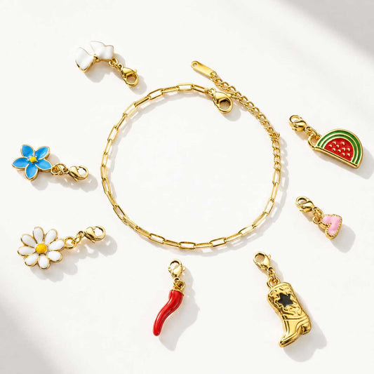 Goldenes Charm-Armband Basis mit verschiedenen Emaille-Charms – Gänseblümchen, Blume, Herz, Schleife, Chili, Cowboystiefel und Wassermelone auf weißem Hintergrund
