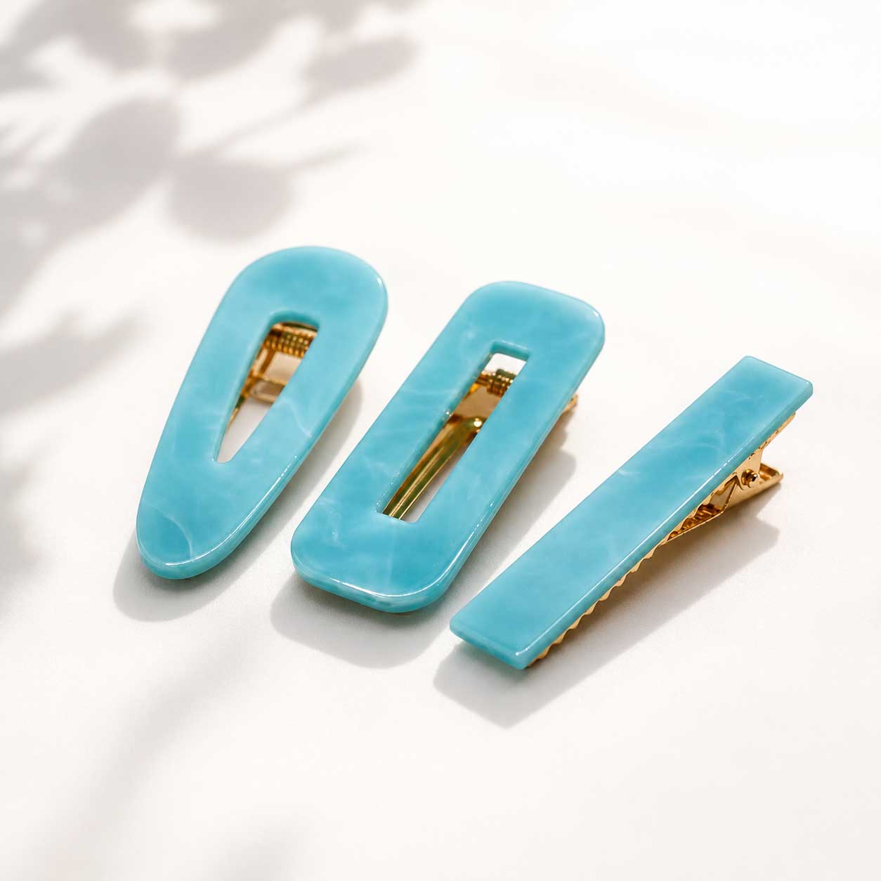 Türkisfarbenes Haarspangen-Set 3 Stück auf weißem Hintergrund, blaue Acryl-Haarclips in oval, rechteckig und eckig mit goldenem Clip
