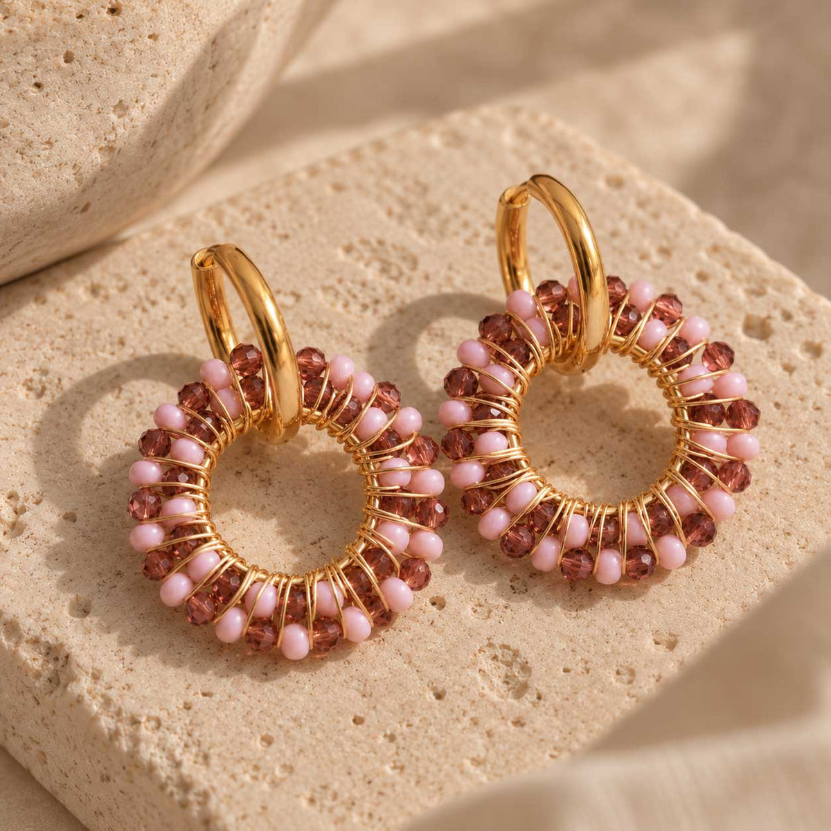 Blush Beaded Hoops – goldene Creolen mit rosa und burgunderroten Kristallperlen, Draufsicht auf Naturstein
