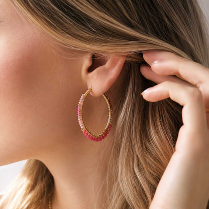 Goldene ovale Creolen mit pinken Kristallperlen am Ohr getragen, Perlen-Ohrringe mit Rosa-Pink-Farbverlauf und goldenem Klappverschluss
