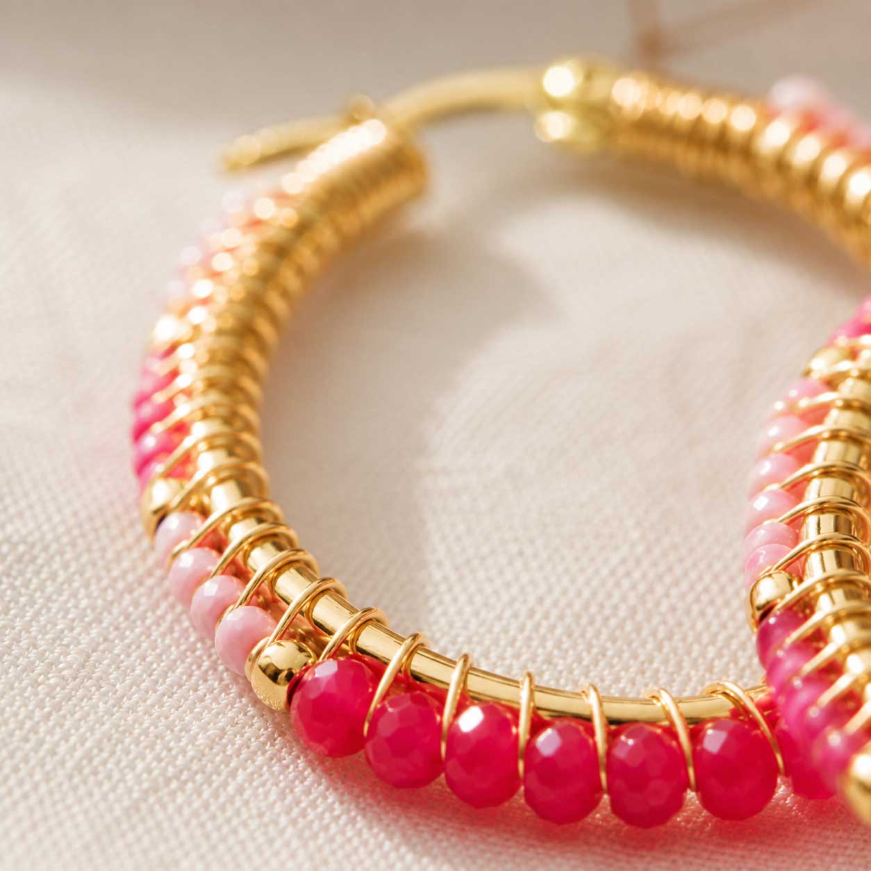 Nahaufnahme goldener Creolen mit pinken und hellrosa facettierten Kristallperlen, Detailansicht der Perlenwicklung und vergoldeten Öse

