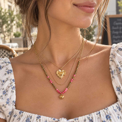 Goldene dreireihige Halskette aus Edelstahl am Hals getragen, mit facettierten Elementen und korallfarbenen Herzen als femininer Layering-Schmuck
[AI]