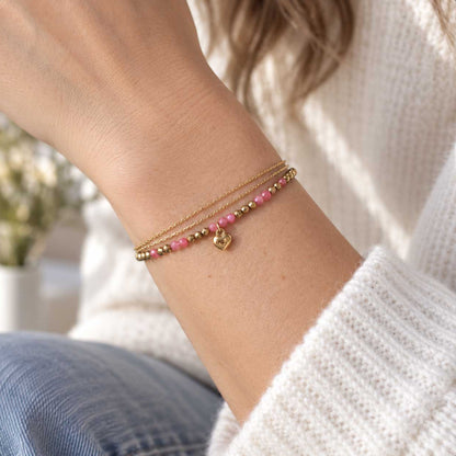 Goldenes dreireihiges Armband aus Edelstahl am Handgelenk getragen, mit facettierten Elementen und Herzdetail als femininer Layering-Schmuck
[AI]