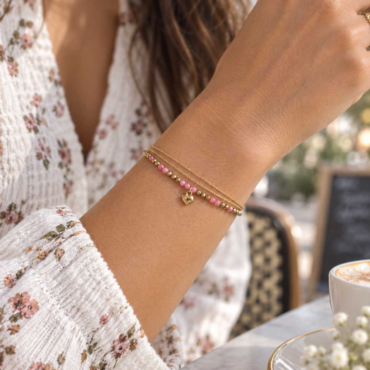 Goldenes dreireihiges Armband aus Edelstahl am Handgelenk getragen, mit facettierten Elementen und Herzdetail als femininer Layering-Schmuck
[AI]