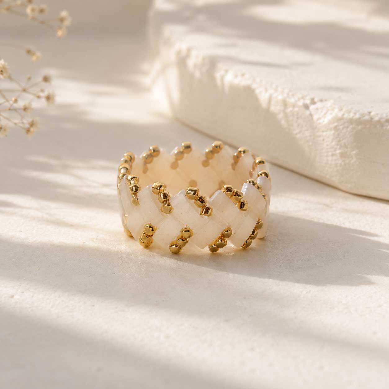 Cremefarbener Miyuki-Perlenring mit goldenen Rocailles in Flechtmuster, handgefertigter Beaded Ring in Creme-Gold auf grauem Untergrund
