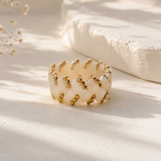 Cremefarbener Miyuki-Perlenring mit goldenen Rocailles in Flechtmuster, handgefertigter Beaded Ring in Creme-Gold auf grauem Untergrund
