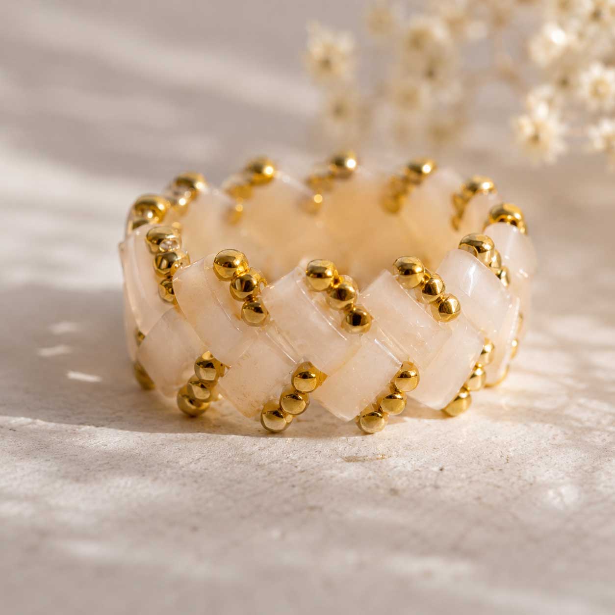 Cremefarbener Miyuki-Perlenring mit goldenen Rocailles in Flechtmuster, handgefertigter Beaded Ring in Creme-Gold auf hellem Untergrund mit Schleierkraut im Sonnenlicht
