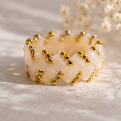 Cremefarbener Miyuki-Perlenring mit goldenen Rocailles in Flechtmuster, handgefertigter Beaded Ring in Creme-Gold auf hellem Untergrund mit Schleierkraut im Sonnenlicht
