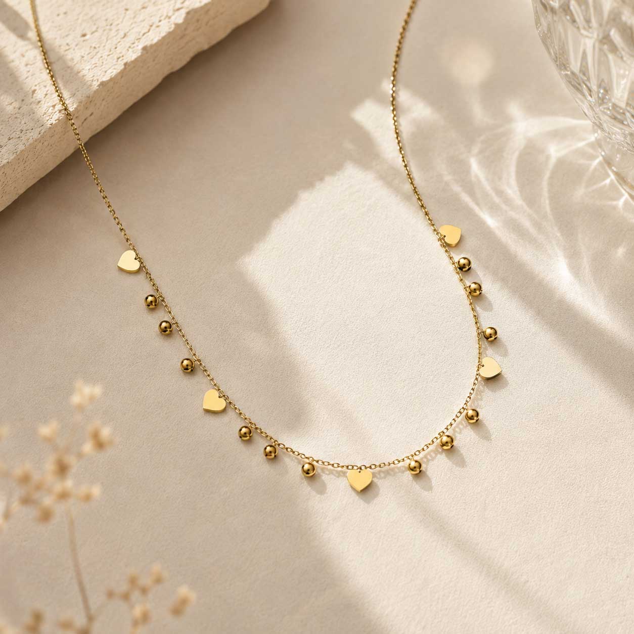 Goldene Halskette mit Herz- und Kugelanhängern – Blushheart Halskette von Saltyblush, filigrane Goldkette mit 4 Herzcharms und 7 Kugelanhängern, Flatlay auf hellem Hintergrund
