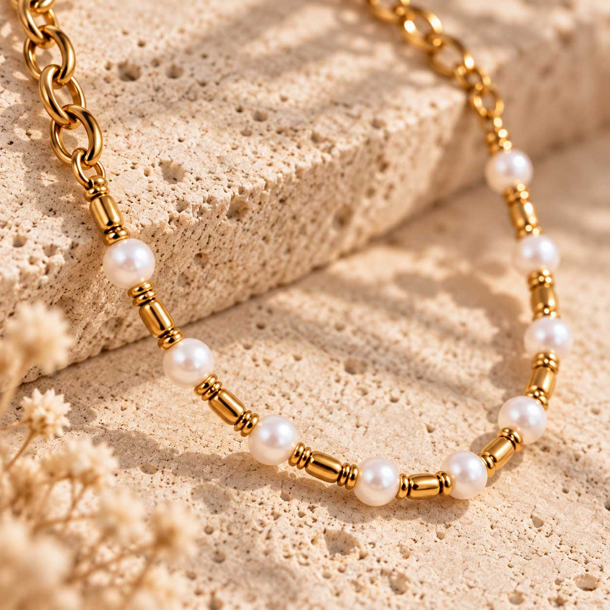 Coastal Pearl goldene Halskette Detailaufnahme – weiße runde Perlen abwechselnd mit goldenen Zylinder-Spacern und O-Ring-Gliedern aus vergoldetem Edelstahl, auf Travertin-Stein mit Trockenblumen, Makroansicht
