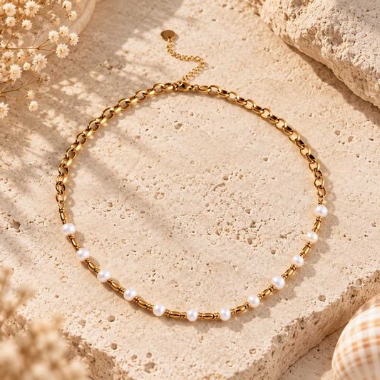 Coastal Pearl goldene Halskette Produktfoto – vollständige Kette aus O-Ring-Gliedern, weißen Perlen und goldenen Zylinder-Spacern mit Karabinerverschluss und Verlängerungskette, auf Travertin-Stein mit Muscheln und Schleierkraut
