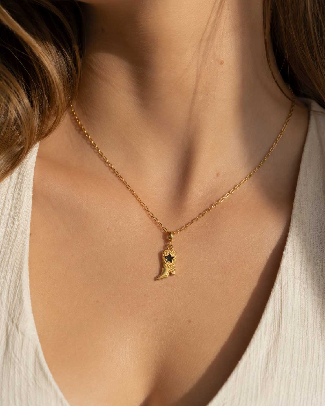 Frau in weißem Oberteil trägt goldene Halskette mit Cowboy Boot Charm am Décolleté – Saltyblush
