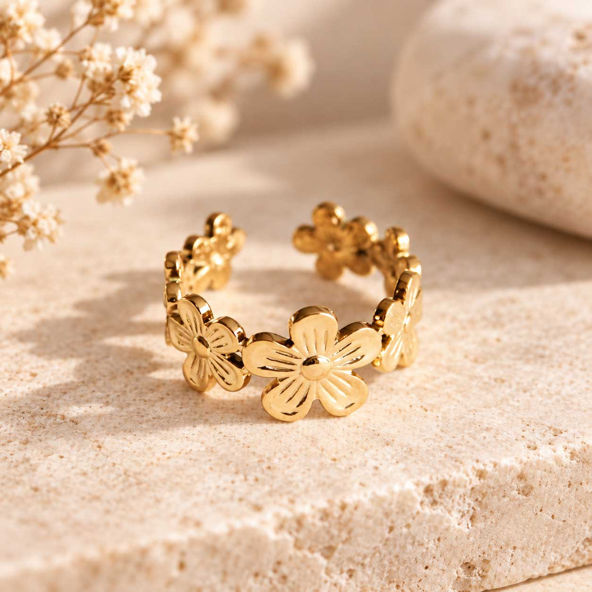 Daisy Kiss goldener Ring – offener Blumenring aus vergoldetem Edelstahl mit mehreren 5-Blatt-Blüten, auf Travertin-Stein mit Trockenblumen, Produktfoto

