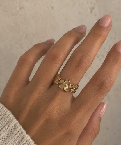 Daisy Kiss goldener Ring getragen – Nahaufnahme Frauenhand mit nude Nägeln, offener Blumenring aus vergoldetem Edelstahl am Mittelfinger, heller Hintergrund
[AI]
