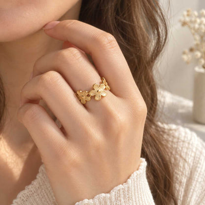Daisy Kiss goldener Ring getragen – brünette Frau, Nahaufnahme Hand am Gesicht, vergoldeter offener Blumenring am Finger, weißer Strickpullover, warmes Licht
[AI]