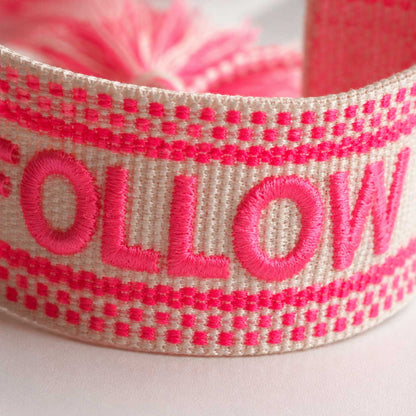 Nahaufnahme gestickter Schriftzug „Follow Your Heart" auf gewebtem Armband in Pink und Creme – Saltyblush
