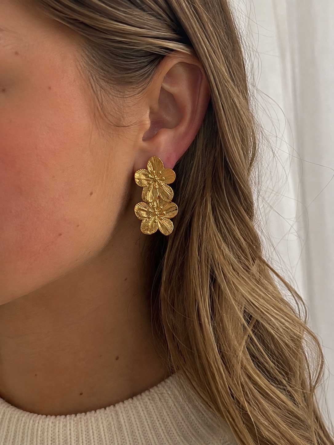 Frau mit langen blonden Haaren trägt die Golden Blossom Ohrringe mit doppeltem Blütendesign am Ohr – Saltyblush
