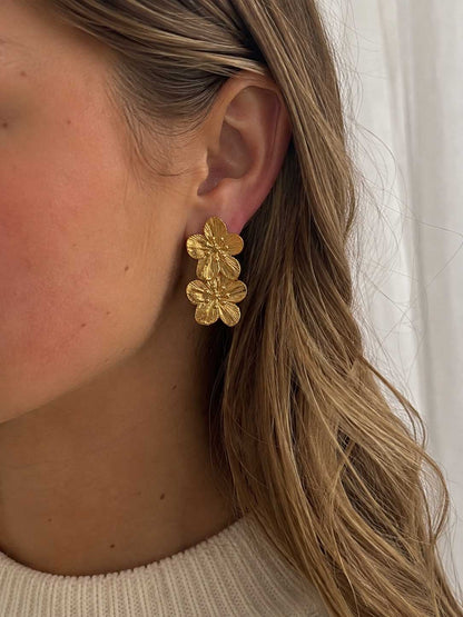 Frau mit langen blonden Haaren trägt die Golden Blossom Ohrringe mit doppeltem Blütendesign am Ohr – Saltyblush
