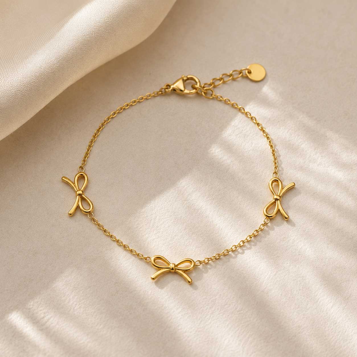Goldenes Armband mit Schleifenanhängern – Golden Bow Armband von Saltyblush, filigrane Goldkette mit 3 Schleifencharms, Flatlay auf hellem Hintergrund
