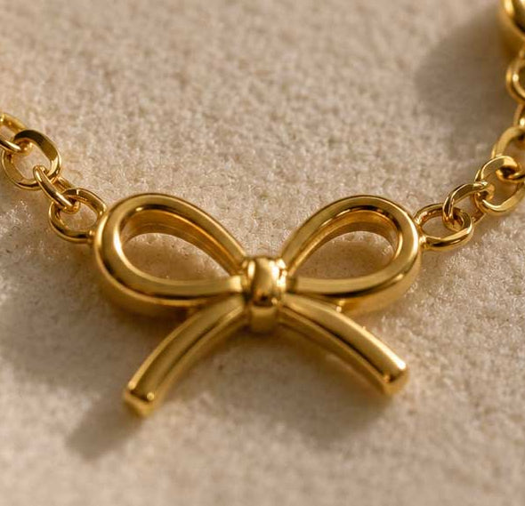 Nahaufnahme goldener Schleifenanhänger – Golden Bow Armband von Saltyblush, glänzender 3D-Schleifencharm an feiner Goldkette, Detailansicht
