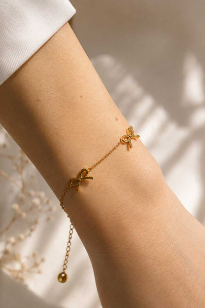 Golden Bow Armband am Handgelenk – goldenes Schleifenarmband von Saltyblush getragen, 3 filigrane Schleifencharms zu weißem Outfit, feminines Schmuckstück
