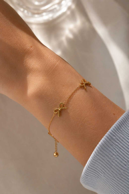 Golden Bow Armband Lifestyle – goldenes Schleifenarmband von Saltyblush am Handgelenk, eleganter Look zu hellblauem Strickpullover im Sonnenlicht
