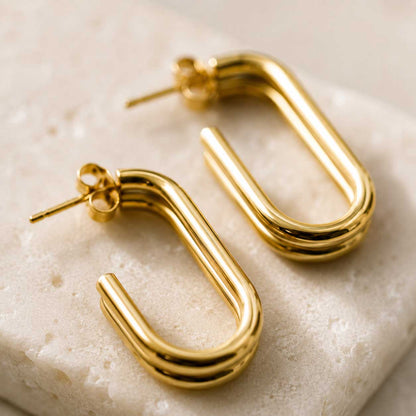 Nahaufnahme goldener U-förmiger Ohrringe mit doppeltem Steg auf hellem Marmor – Golden Curve U-Shape von Saltyblush
