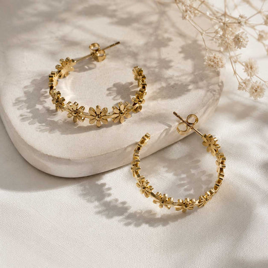 Goldene Creolen mit Gänseblümchen-Muster auf hellem Steinuntergrund mit Trockenblumen – Golden Daisy von Saltyblush
