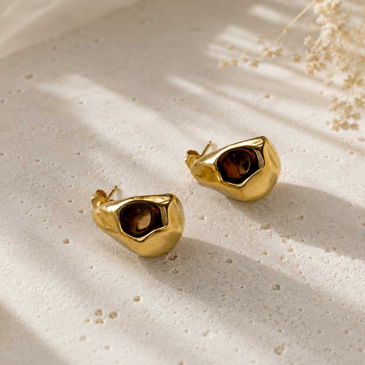 Zwei goldene Drop Ohrstecker aus Edelstahl mit braunem Stein auf cremefarbenem Untergrund – Saltyblush
