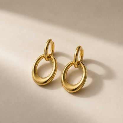 Goldene Ohrringe mit doppeltem Oval-Ring aus Edelstahl auf cremefarbenem Hintergrund – Golden Flow von Saltyblush
