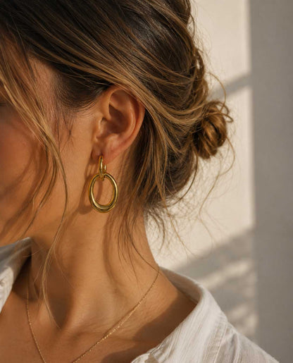 Golden Flow goldene Ohrringe mit ovalem Doppelring am Ohr getragen mit weißem Hemd im Sonnenlicht – Saltyblush
