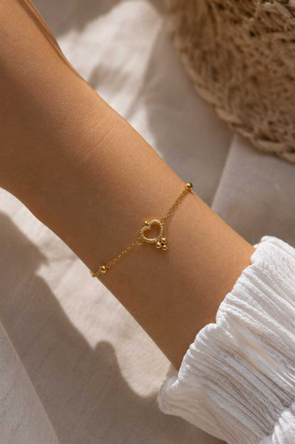 Golden Glow Armband am Handgelenk – goldenes Herzarmband von Saltyblush getragen, offener Herzcharm mit Kugeldetails zu weißem Strickoberteil im Sonnenlicht
