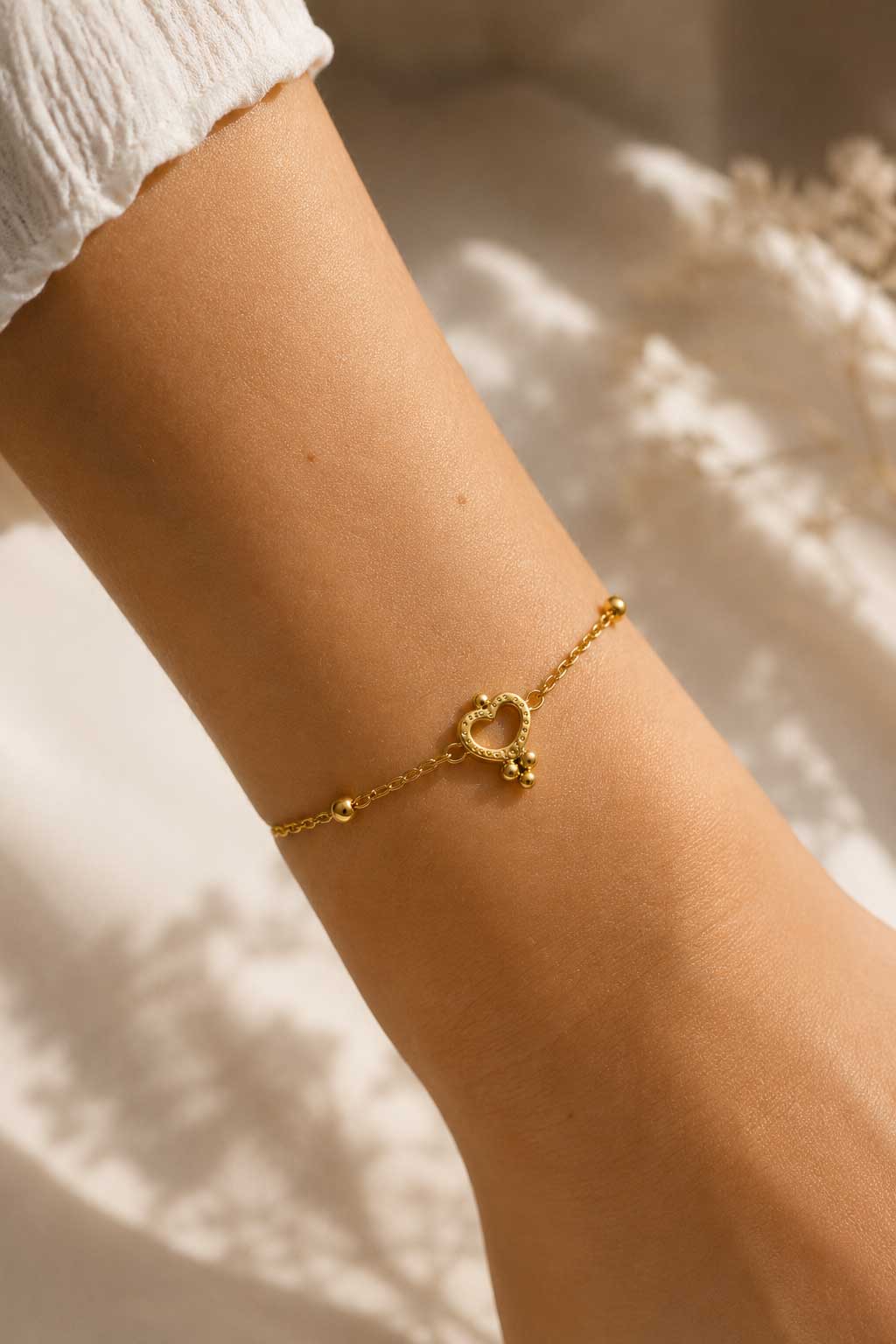 Golden Glow Armband Lifestyle – goldenes Herzarmband von Saltyblush am Handgelenk, eleganter Look zu weißem Outfit, feminines Schmuckstück im Sonnenlicht
