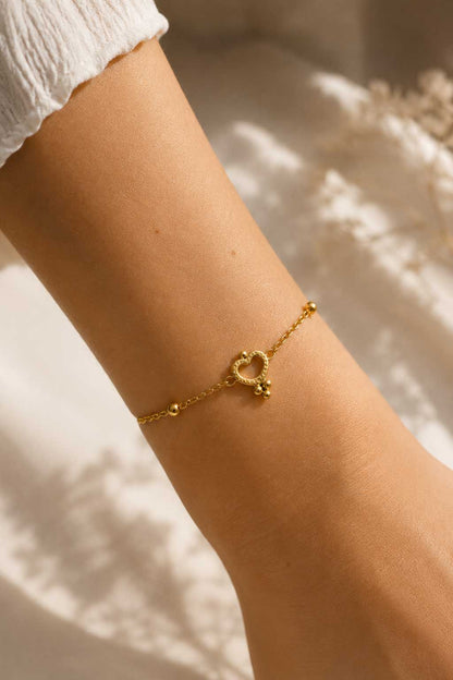Golden Glow Armband Lifestyle – goldenes Herzarmband von Saltyblush am Handgelenk, eleganter Look zu weißem Outfit, feminines Schmuckstück im Sonnenlicht
