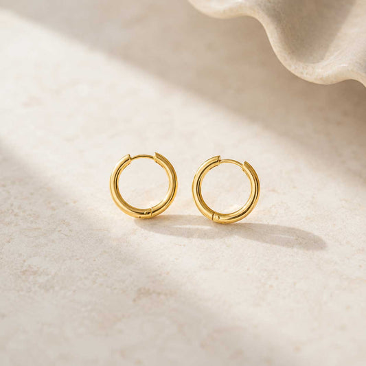 Zwei goldene Hoop Ohrringe aus Edelstahl auf hellem Muscheluntergrund – Saltyblush
