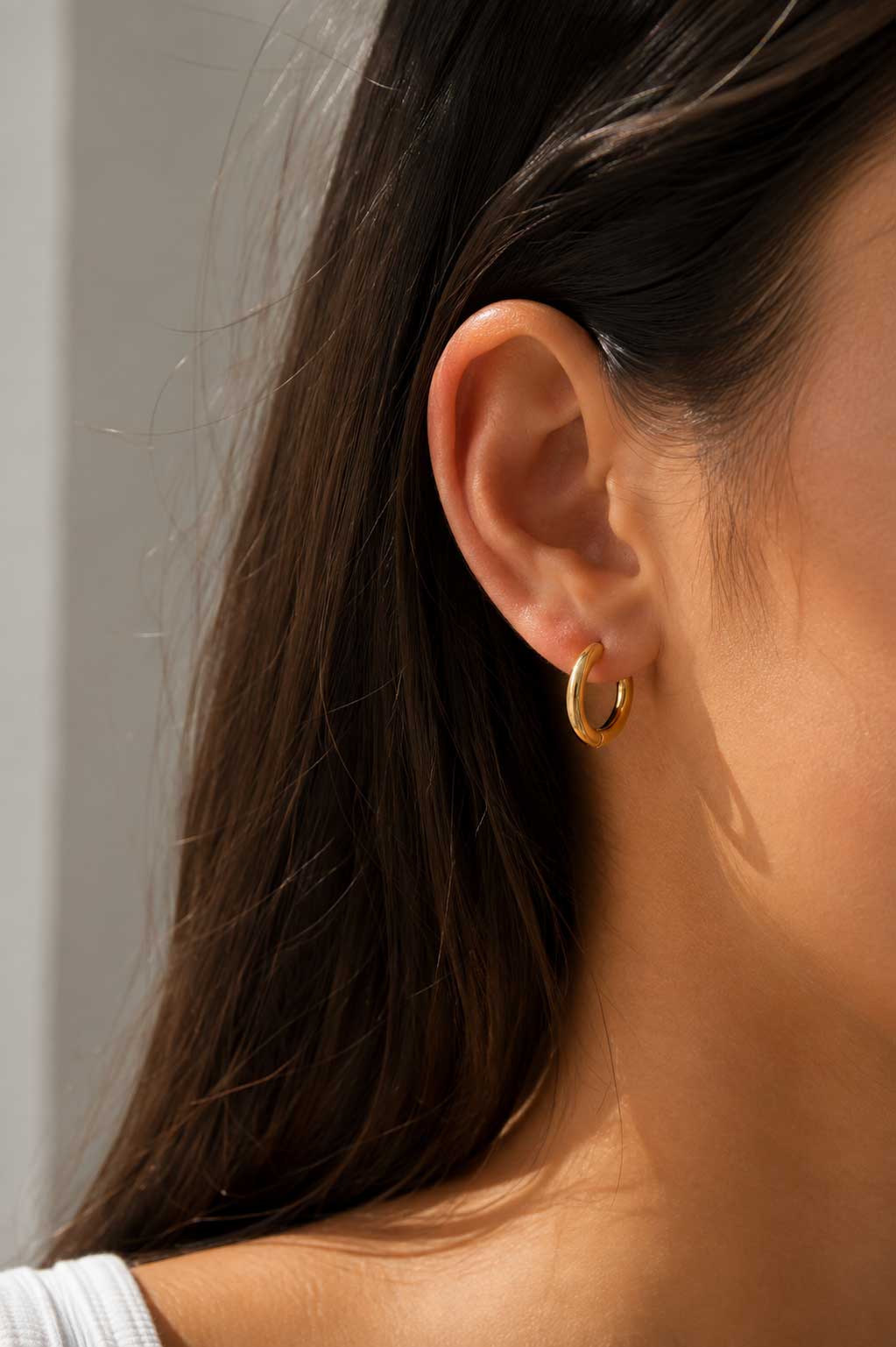 Brünette Frau trägt goldene Hoop Creolen aus Edelstahl am Ohr – Lifestyle-Aufnahme – Saltyblush
