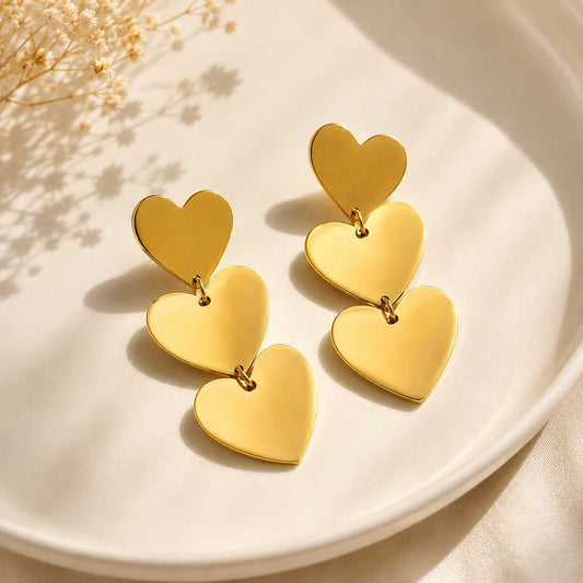 Golden Love goldene Ohrringe mit drei Herz-Elementen auf weißem Teller
