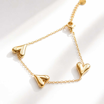 Goldenes Armband mit drei Herz-Anhängern auf weißem Hintergrund, vergoldete Gliederkette mit Karabinerverschluss
