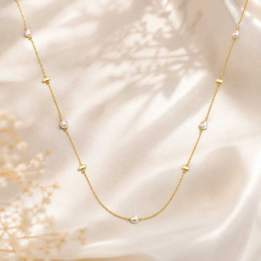 Golden Pearl Halskette Flatlay – goldene Perlenkette von Saltyblush, filigrane Goldkette mit 5 weißen Perlen und goldenen Plättchen, auf weißem Stoff mit Trockenblumen
