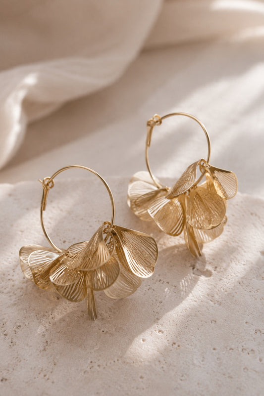 Goldene Creolen mit mehrlagigen Blütenblatt-Anhängern auf hellem Steinuntergrund – Golden Petal Hoops von Saltyblush
