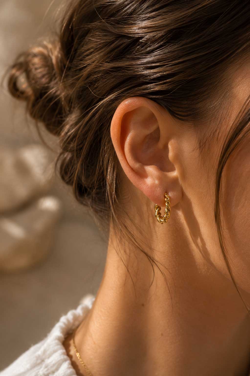 Brünette Frau trägt goldene gedrehte Creolen aus Edelstahl am Ohr – Lifestyle-Aufnahme – Saltyblush
