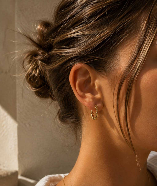 Frau mit hochgestecktem Haar trägt goldene Twist Creolen aus Edelstahl – elegante Lifestyle-Aufnahme – Saltyblush
