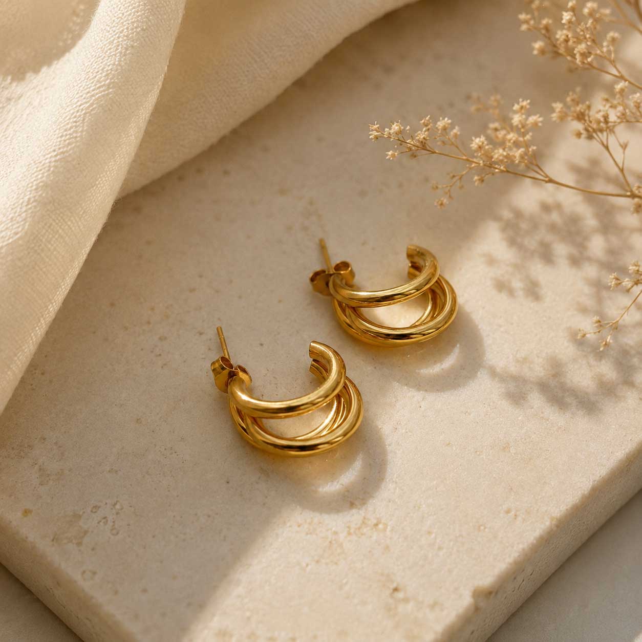Goldene dreilagige Creolen aus Edelstahl auf cremefarbenem Stein mit Seidenstoff und Trockenblumen – Golden Wave Hoops von Saltyblush
