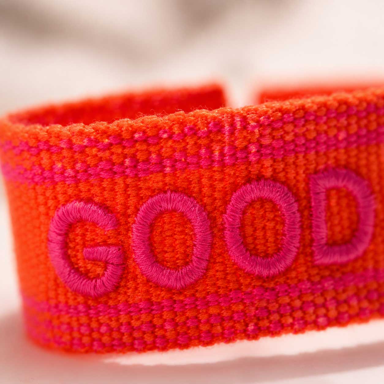 Nahaufnahme gestickter Schriftzug „Good Vibes" in Neonpink auf orangenem Webarmband – Saltyblush Modeschmuck
