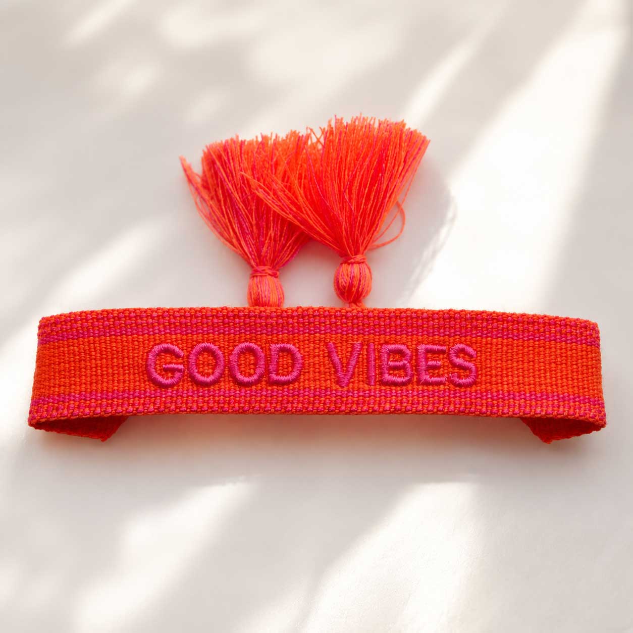 Good Vibes Statement Armband aufgeklappt mit zwei orangenen Quasten und pinkem Schriftzug – Saltyblush
