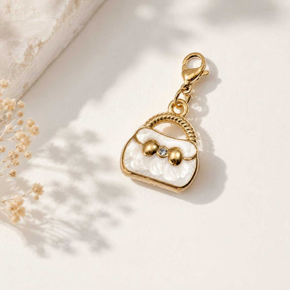 Goldener Handtaschen-Charm in Weiß mit Kristallstein und Karabinerverschluss auf cremefarbenem Hintergrund mit Trockenblumen – Saltyblush
