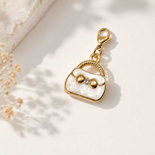 Goldener Handtaschen-Charm in Weiß mit Kristallstein und Karabinerverschluss auf cremefarbenem Hintergrund mit Trockenblumen – Saltyblush
