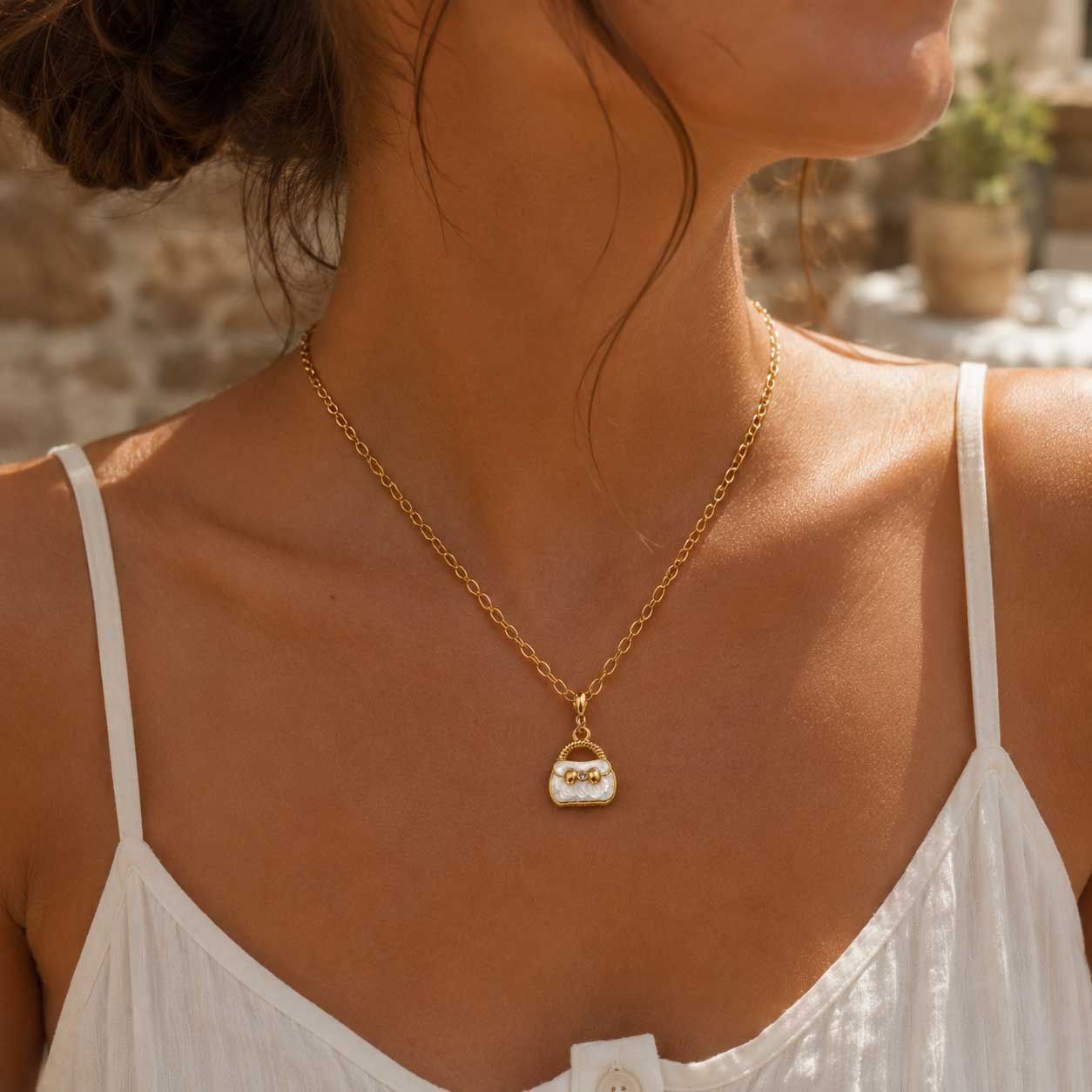 Frau in weißem Trägerkleid trägt goldene Halskette mit weißem Handtaschen-Charm am Décolleté – Saltyblush
